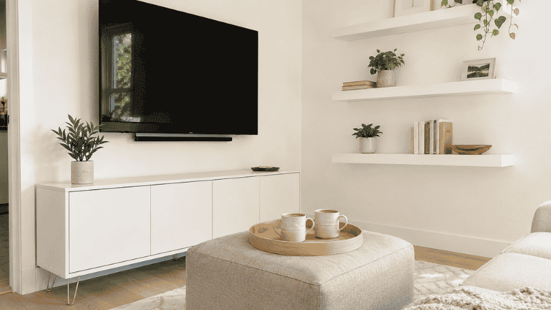 A small living room with organized storage — a closed-door media console, storage ottoman with tray, and floating shelves — showing 80% concealed and 20% display storage balance
