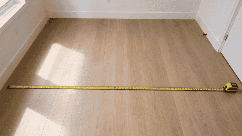 Person measuring a small living room floor with a yellow tape measure before arranging furniture