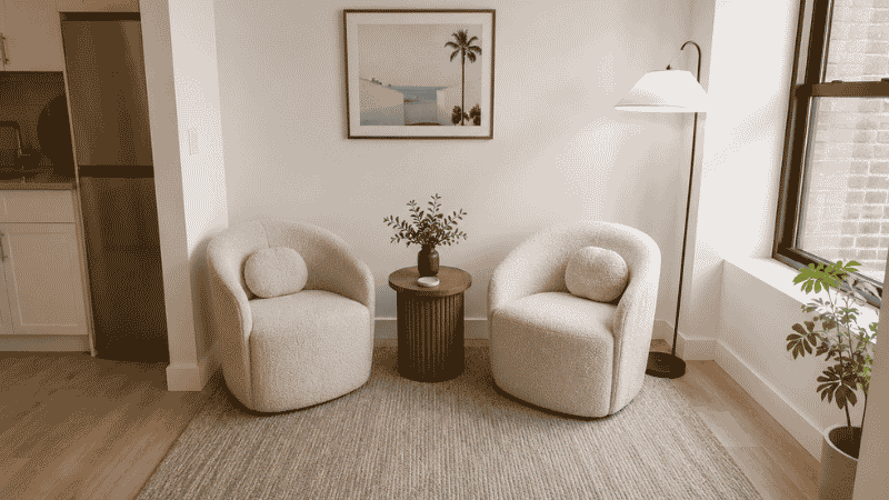 Studio apartment living area with two bouclé accent chairs angled toward each other around a small round ottoman, no sofa