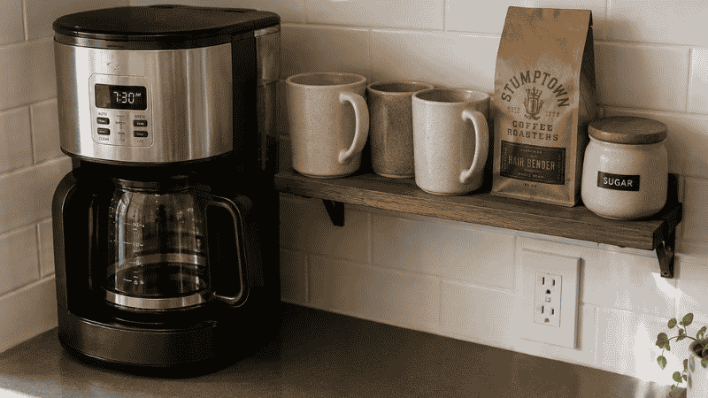 A small apartment kitchen showing coffee mugs stored directly beside the coffee maker on an open shelf, demonstrating the 30-second proximity rule where items are stored within arm's reach of where they are used
