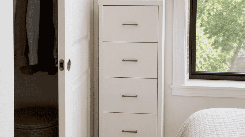 A small bedroom showing a slim 20-inch wide dresser placed in the gap between a closet door frame and a window wall, the closet door shown open at 90 degrees clearing the dresser front by 4 inches
