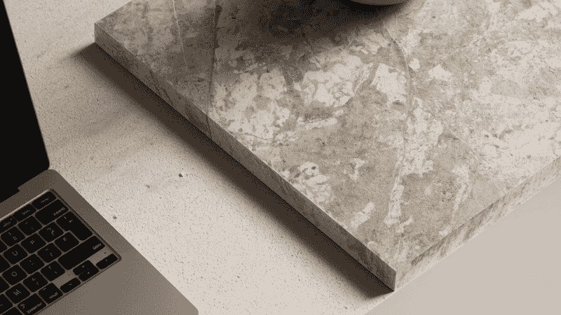 Close-up detail of a matte sintered stone dining table surface with marble-like veining, supporting a laptop and a ceramic vase, showing scratch-resistant texture.