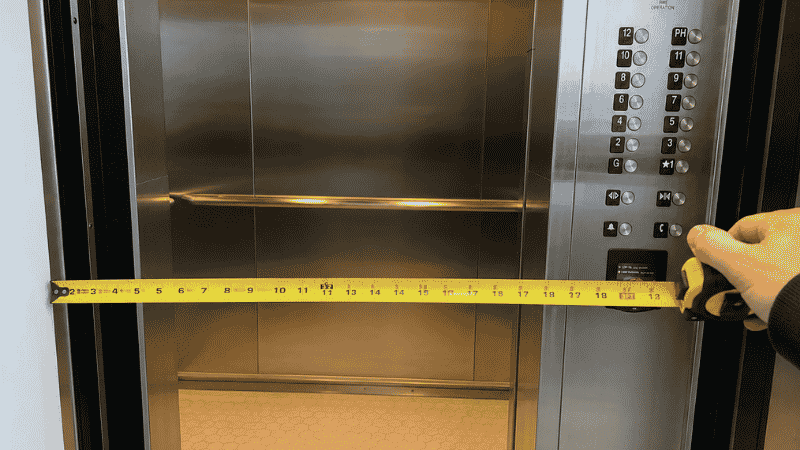 A tape measure checking the interior width of a residential apartment elevator at 36 inches, showing the measurement check needed before ordering a sofa for delivery to an upper-floor apartment

