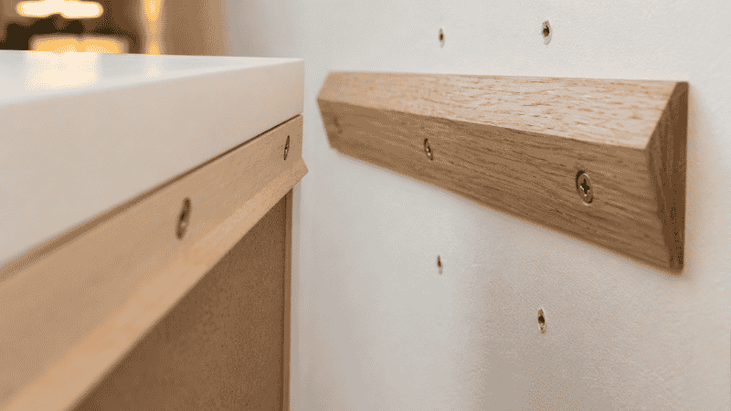 Close-up of a French cleat system showing the wall-mounted angled board and the matching angled board on the console back, with the console hanging securely on the wall cleat — demonstrating the renter-friendly installation method requiring minimal wall holes