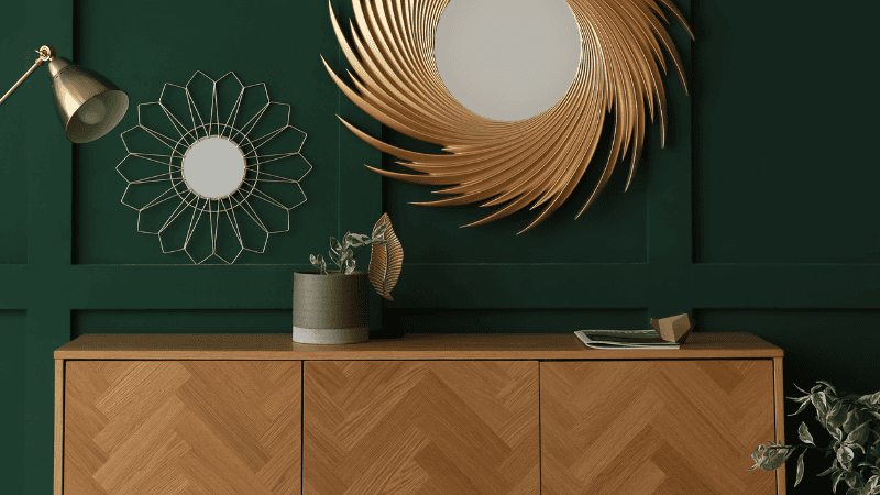A minimalist fluted oak sideboard with brass legs positioned against a sage green wall, styled with a modern lamp and a large circular mirror in a contemporary dining room.